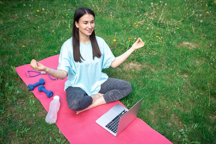 Woman meditating with a laptop in a park